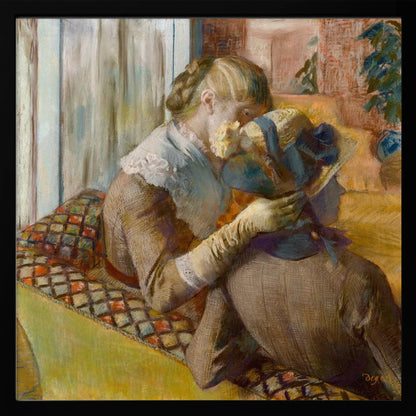 A framed Impressionist painting by Edgar Degas depicting two women. One woman, with blonde hair tied back, adjusts a hat with a blue ribbon on the other woman who is sitting with her back mostly to the viewer on a colorful patterned sofa. Print