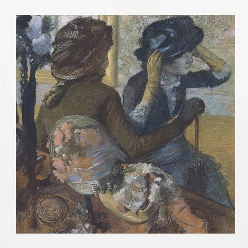 A framed impressionist painting by Edgar Degas, 'The Millinery Shop', depicting two women. One woman, seen from the back, wears a brown coat and hat, while the other tries on a dark blue hat, adjusting it with her gloved hands. Colorful hats are displayed in the foreground. Print