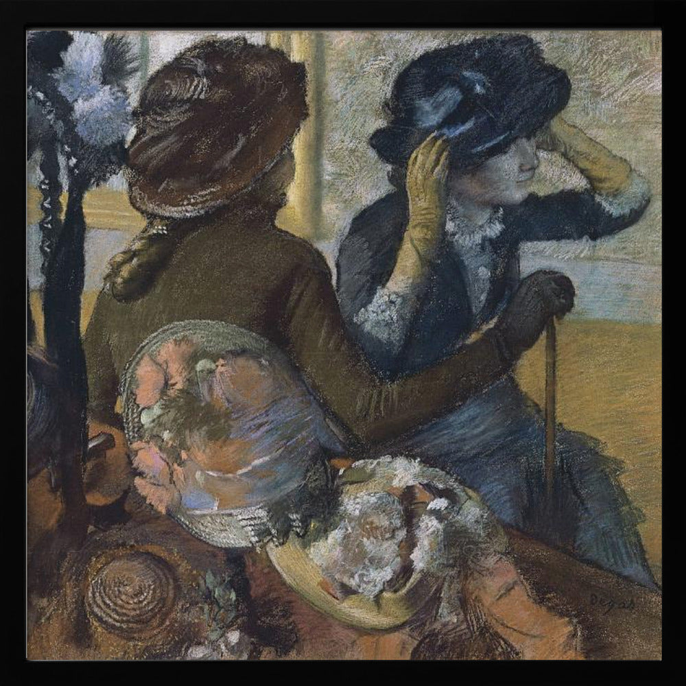 A framed impressionist painting by Edgar Degas, 'The Millinery Shop', depicting two women. One woman, seen from the back, wears a brown coat and hat, while the other tries on a dark blue hat, adjusting it with her gloved hands. Colorful hats are displayed in the foreground. Print