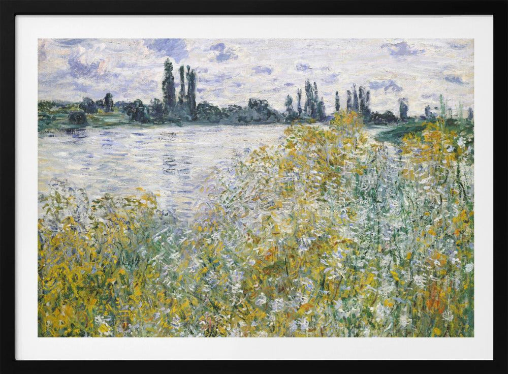 An impressionist landscape painting of a riverbank covered in yellow and white wildflowers. A calm river reflects the cloudy sky, and the opposite bank is lined with tall, dark poplar trees. The artwork is displayed in a silver frame. Artwork
