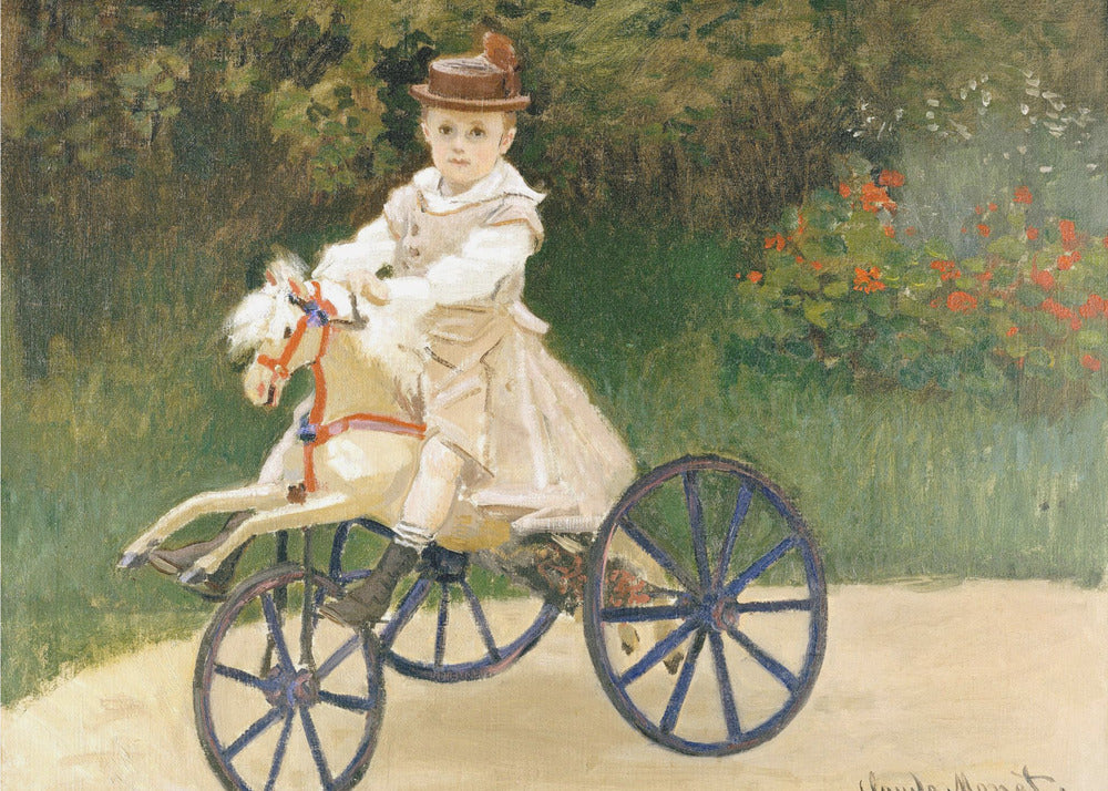 An Impressionist painting by Claude Monet depicting his son, Jean, riding a toy horse tricycle. The young boy wears a brown hat and a light-colored outfit, sitting on a white hobby horse with large blue wheels, set against a lush green garden background. Decor