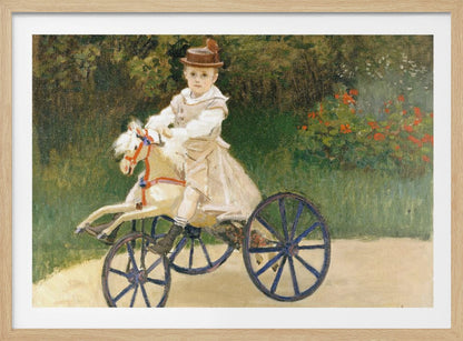 An Impressionist painting by Claude Monet depicting his son, Jean, riding a toy horse tricycle. The young boy wears a brown hat and a light-colored outfit, sitting on a white hobby horse with large blue wheels, set against a lush green garden background. Decor