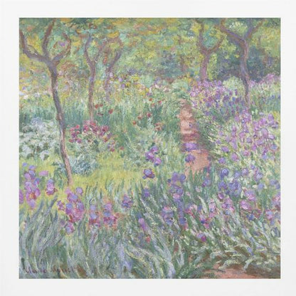 An impressionist painting by Claude Monet, 'The Artist's Garden at Giverny,' set in a light wood frame. The artwork depicts a lush, vibrant garden with a path winding through it. The foreground is dominated by purple irises and tall green leaves, while the background features trees and a mix of colorful flowers in shades of red, yellow, and white, all rendered with visible, textured brushstrokes. Print