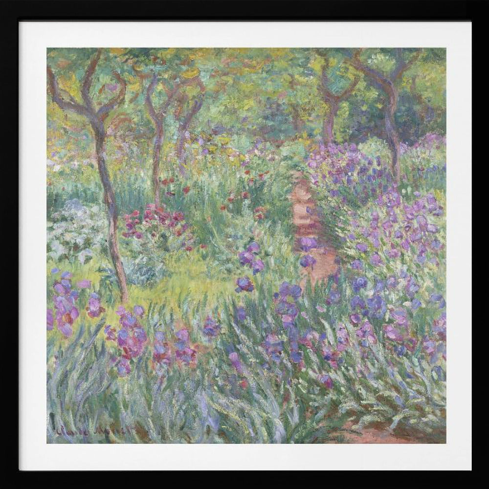 An impressionist painting by Claude Monet, 'The Artist's Garden at Giverny,' set in a light wood frame. The artwork depicts a lush, vibrant garden with a path winding through it. The foreground is dominated by purple irises and tall green leaves, while the background features trees and a mix of colorful flowers in shades of red, yellow, and white, all rendered with visible, textured brushstrokes. Print