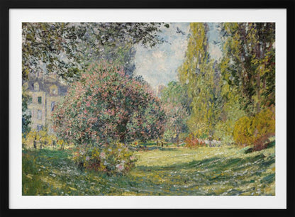An impressionist painting by Claude Monet titled 'The Parc Monceau' displayed in a silver frame. The scene depicts a sunlit park with lush green grass, a large pink-flowering bush, and tall, leafy trees under a pale blue sky. Decor
