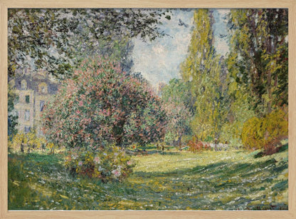 An impressionist painting by Claude Monet titled 'The Parc Monceau' displayed in a silver frame. The scene depicts a sunlit park with lush green grass, a large pink-flowering bush, and tall, leafy trees under a pale blue sky. Decor