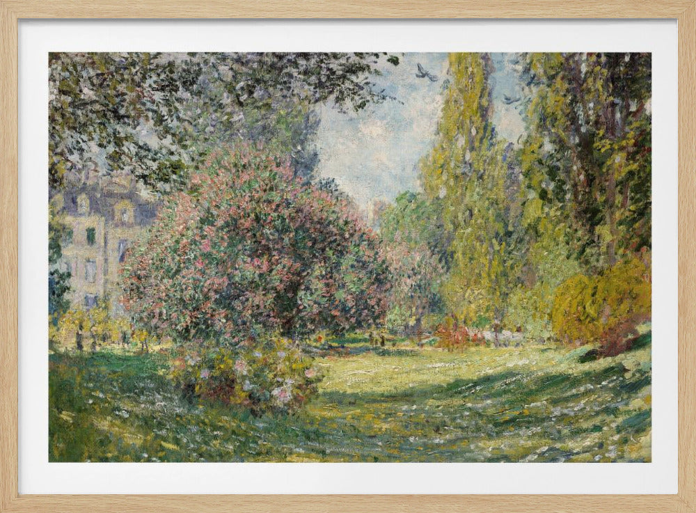 An impressionist painting by Claude Monet titled 'The Parc Monceau' displayed in a silver frame. The scene depicts a sunlit park with lush green grass, a large pink-flowering bush, and tall, leafy trees under a pale blue sky. Decor