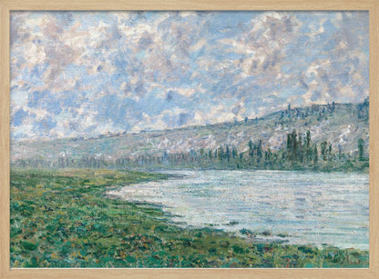An Impressionist painting by Claude Monet, 'The Seine at Vétheuil', depicting a tranquil landscape. In the foreground, a lush green riverbank meets the calm, reflective water. A distant, soft-focus hillside rises under a vast sky filled with puffy white and grey clouds against a light blue background. The artwork is characterized by visible, textured brushstrokes and is displayed in a modern silver frame. Artwork