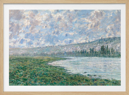 An Impressionist painting by Claude Monet, 'The Seine at Vétheuil', depicting a tranquil landscape. In the foreground, a lush green riverbank meets the calm, reflective water. A distant, soft-focus hillside rises under a vast sky filled with puffy white and grey clouds against a light blue background. The artwork is characterized by visible, textured brushstrokes and is displayed in a modern silver frame. Artwork
