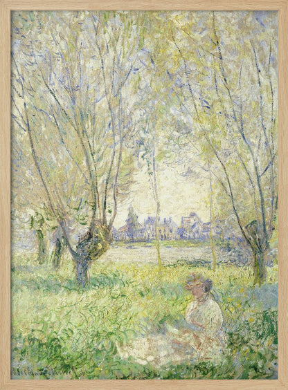 An Impressionist painting, 'Springtime' by Claude Monet, showing a woman in a hat sitting in a sunlit green field. Slender trees with light green foliage frame a view of a village across a river, evoking a peaceful spring day. The artwork is presented in a simple black frame. Artwork