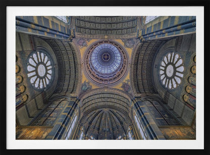 An upward-looking view of the highly ornate vaulted ceiling of a grand cathedral, featuring a central glass dome, large rose windows, and intricate gold and blue details, all framed in silver. Poster