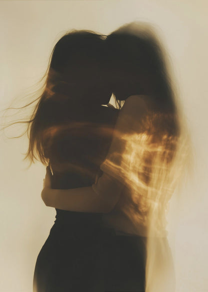 An artistic, long-exposure photograph of two silhouetted figures embracing. Their forms are blurred with motion, and streaks of warm, golden light wash over them against a soft, off-white background, creating a dreamy and intimate mood. Decor
