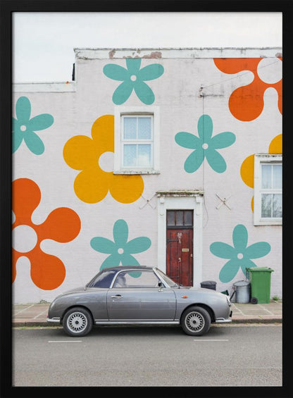 A retro-style gray convertible parked on a city street in front of a building with a large, colorful pop-art mural of stylized flowers in orange, yellow, and turquoise. Decor