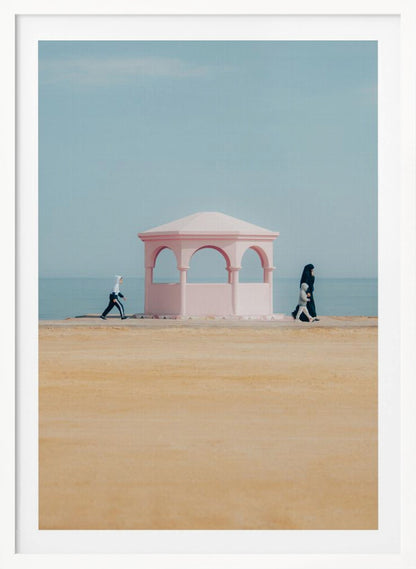 A minimalist photograph of a coastal scene with a pastel color palette. A pink arched gazebo sits on a promenade with the blue sea and sky in the background. A large expanse of beige sand is in the foreground. Two figures in hijabs walk in opposite directions on either side of the gazebo, one with a small child. Decor