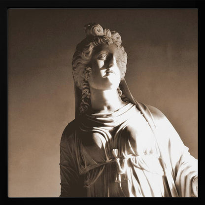 A framed, sepia-toned photograph of a classical marble bust of a woman. She looks upwards and to the side, illuminated by a strong light that casts dramatic shadows across her face and draped clothing. The photo is enclosed in a simple, light wood frame. Print