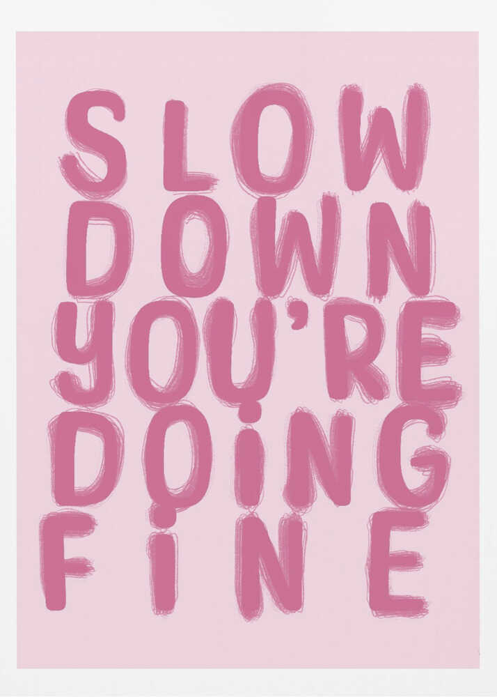 A framed art print featuring the phrase 'SLOW DOWN YOU'RE DOING FINE' in a bold, dark pink, brush-stroke font. The words are stacked vertically against a light pink background, all enclosed within a simple black frame. Artwork