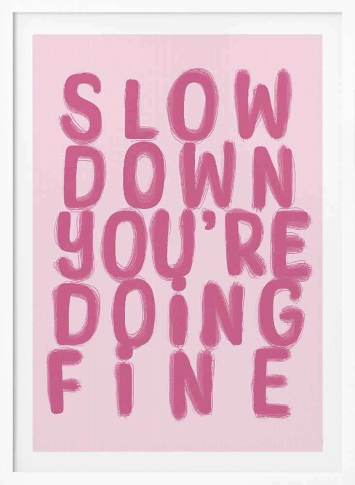 A framed art print featuring the phrase 'SLOW DOWN YOU'RE DOING FINE' in a bold, dark pink, brush-stroke font. The words are stacked vertically against a light pink background, all enclosed within a simple black frame. Artwork