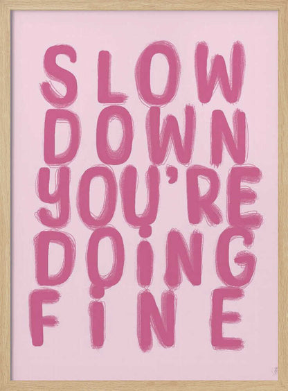 A framed art print featuring the phrase 'SLOW DOWN YOU'RE DOING FINE' in a bold, dark pink, brush-stroke font. The words are stacked vertically against a light pink background, all enclosed within a simple black frame. Artwork