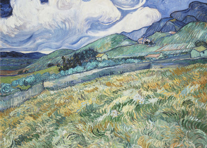 A framed Post-Impressionist painting by Vincent van Gogh depicting a vibrant, rolling landscape. The foreground is filled with swirling brushstrokes of green and yellow fields, leading back to green hills dotted with small houses. In the background, dark blue mountains rise up to meet a dramatic sky filled with large, swirling white clouds against a deep blue. Wall Art
