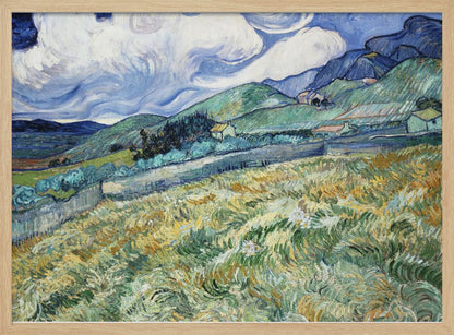 A framed Post-Impressionist painting by Vincent van Gogh depicting a vibrant, rolling landscape. The foreground is filled with swirling brushstrokes of green and yellow fields, leading back to green hills dotted with small houses. In the background, dark blue mountains rise up to meet a dramatic sky filled with large, swirling white clouds against a deep blue. Wall Art