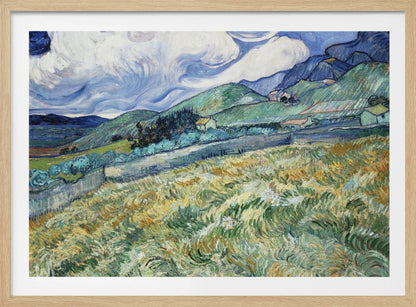 A framed Post-Impressionist painting by Vincent van Gogh depicting a vibrant, rolling landscape. The foreground is filled with swirling brushstrokes of green and yellow fields, leading back to green hills dotted with small houses. In the background, dark blue mountains rise up to meet a dramatic sky filled with large, swirling white clouds against a deep blue. Wall Art
