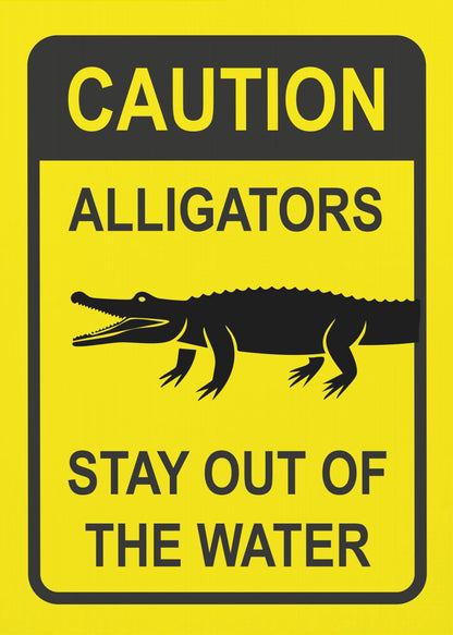 A yellow and black rectangular warning sign in a black frame. The sign reads 'CAUTION ALLIGATORS' at the top, features a black silhouette of an alligator in the center, and says 'STAY OUT OF THE WATER' at the bottom. Decor
