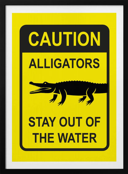 A yellow and black rectangular warning sign in a black frame. The sign reads 'CAUTION ALLIGATORS' at the top, features a black silhouette of an alligator in the center, and says 'STAY OUT OF THE WATER' at the bottom. Decor