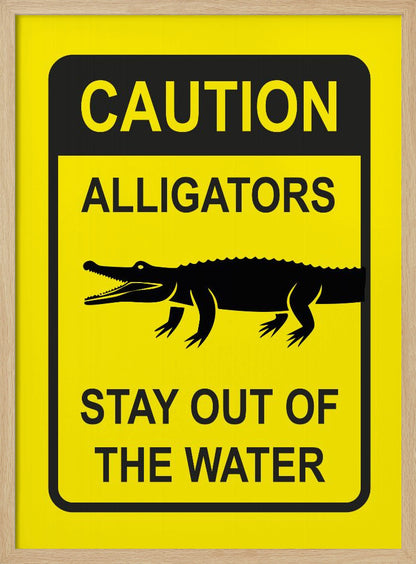 A yellow and black rectangular warning sign in a black frame. The sign reads 'CAUTION ALLIGATORS' at the top, features a black silhouette of an alligator in the center, and says 'STAY OUT OF THE WATER' at the bottom. Decor