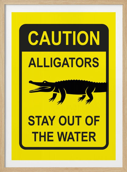 A yellow and black rectangular warning sign in a black frame. The sign reads 'CAUTION ALLIGATORS' at the top, features a black silhouette of an alligator in the center, and says 'STAY OUT OF THE WATER' at the bottom. Decor