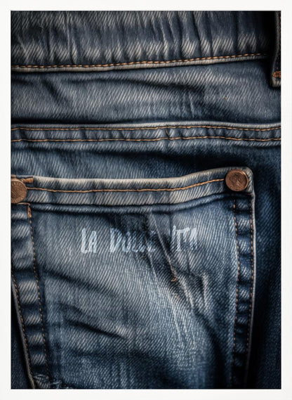 A detailed close-up photograph of a faded blue jean back pocket, showing the texture of the denim, orange stitching, and a copper rivet. Faint white text is stenciled onto the pocket. Poster
