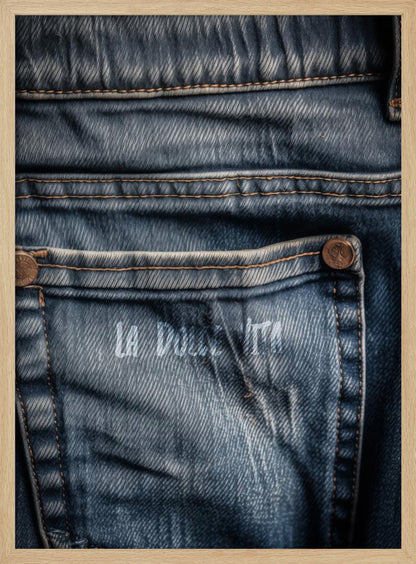 A detailed close-up photograph of a faded blue jean back pocket, showing the texture of the denim, orange stitching, and a copper rivet. Faint white text is stenciled onto the pocket. Poster