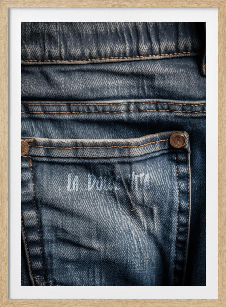 A detailed close-up photograph of a faded blue jean back pocket, showing the texture of the denim, orange stitching, and a copper rivet. Faint white text is stenciled onto the pocket. Poster