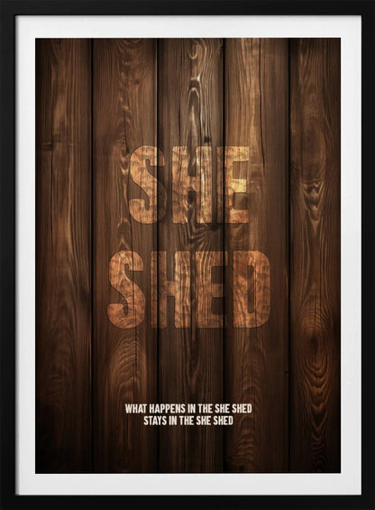 A rustic poster with a dark brown wood panel background. The words 'SHE SHED' are in large, blocky letters with a distressed wood texture. Below, a smaller caption reads 'WHAT HAPPENS IN THE SHE SHED STAYS IN THE SHE SHED'. The poster is displayed in a thin black frame. Print