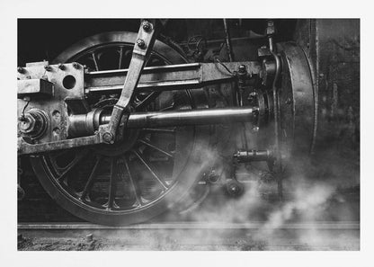 A dramatic, black and white close-up photograph of the wheels and driving rods of a steam locomotive. Puffs of steam rise from the tracks, partially obscuring the lower part of the machinery. Print