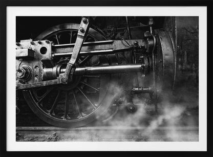 A dramatic, black and white close-up photograph of the wheels and driving rods of a steam locomotive. Puffs of steam rise from the tracks, partially obscuring the lower part of the machinery. Print