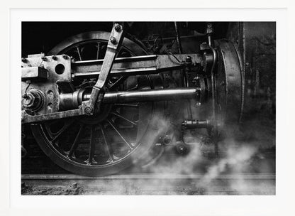 A dramatic, black and white close-up photograph of the wheels and driving rods of a steam locomotive. Puffs of steam rise from the tracks, partially obscuring the lower part of the machinery. Print