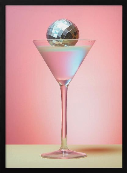 A sleek martini glass filled with an iridescent pink and blue cocktail is centered against a solid pink background. A small, shiny silver disco ball rests on the rim of the glass, completing the festive and stylish composition. Decor