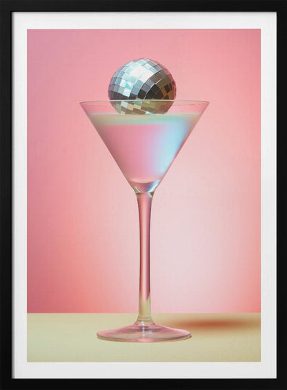 A sleek martini glass filled with an iridescent pink and blue cocktail is centered against a solid pink background. A small, shiny silver disco ball rests on the rim of the glass, completing the festive and stylish composition. Decor