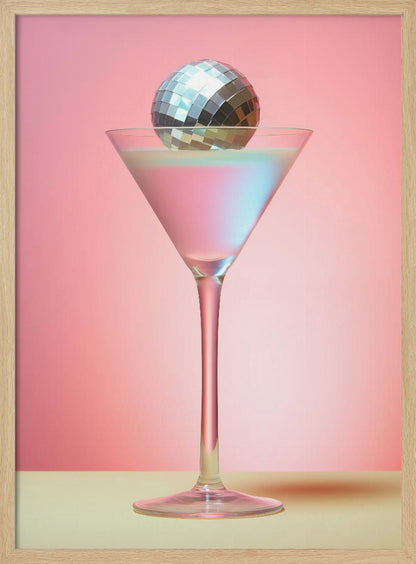 A sleek martini glass filled with an iridescent pink and blue cocktail is centered against a solid pink background. A small, shiny silver disco ball rests on the rim of the glass, completing the festive and stylish composition. Decor