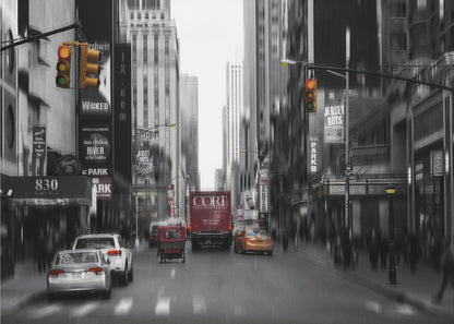 A framed, stylized photograph of a busy New York City street, presented mostly in black and white with a motion blur effect. Pops of color highlight red vehicles and yellow traffic lights, drawing focus down the urban canyon lined with skyscrapers and Broadway signs. Decor