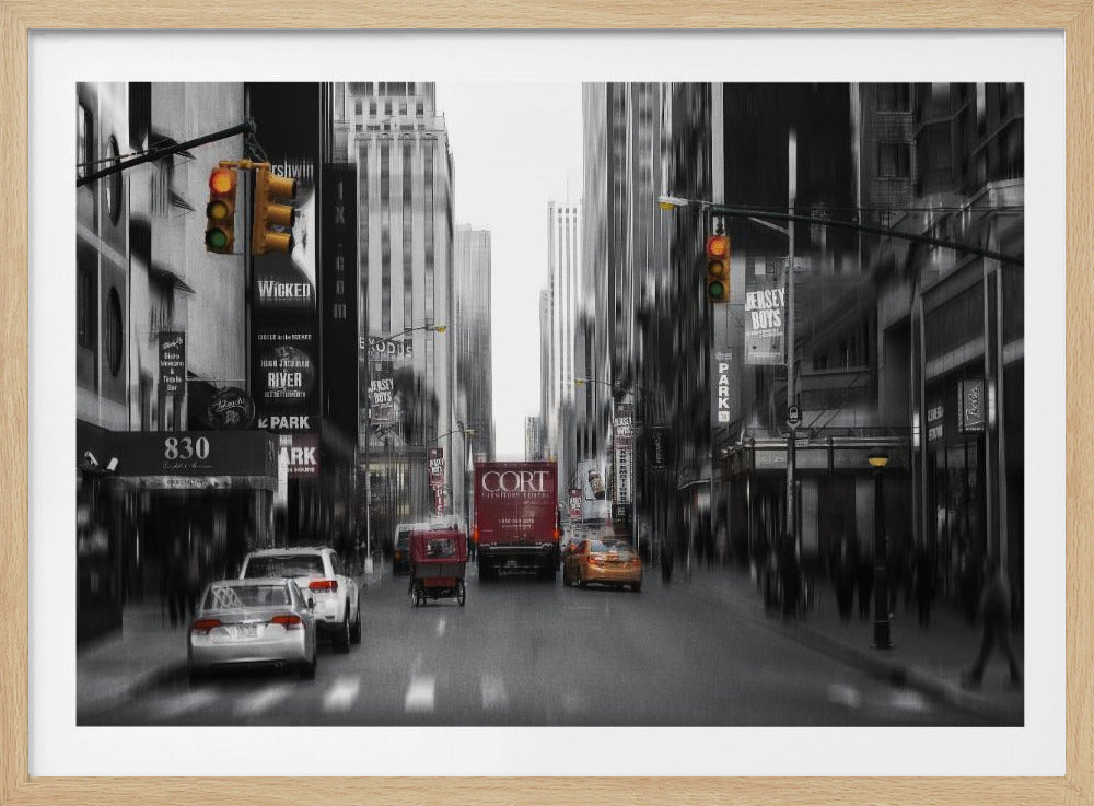 A framed, stylized photograph of a busy New York City street, presented mostly in black and white with a motion blur effect. Pops of color highlight red vehicles and yellow traffic lights, drawing focus down the urban canyon lined with skyscrapers and Broadway signs. Decor