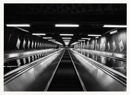 A framed, black and white, low-angle photograph looking up a long, steep, and empty escalator in a subway tunnel. The symmetrical composition uses the shiny metal handrails and rows of overhead lights as leading lines, creating a dramatic sense of depth and perspective. Print