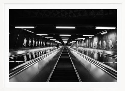 A framed, black and white, low-angle photograph looking up a long, steep, and empty escalator in a subway tunnel. The symmetrical composition uses the shiny metal handrails and rows of overhead lights as leading lines, creating a dramatic sense of depth and perspective. Print