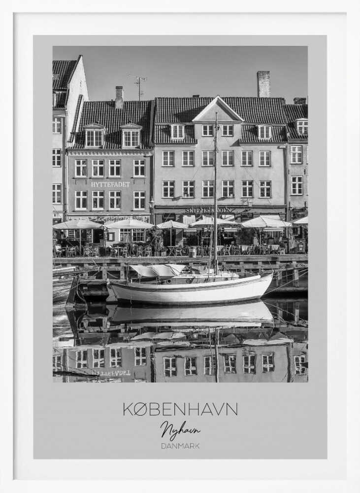 A black and white framed poster of Nyhavn in Copenhagen. The photograph features classic Danish buildings lining a canal, with a sailboat moored in the water. The buildings and boat are perfectly reflected in the still water. At the bottom, text reads 'KØBENHAVN', 'Nyhavn', and 'DANMARK'. Wall Art