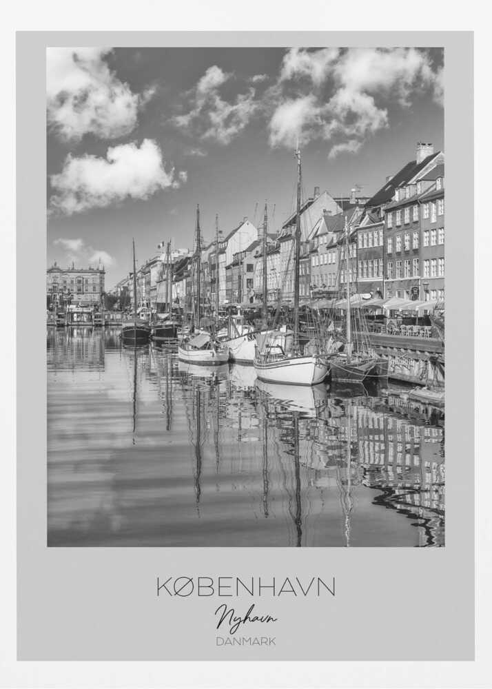A black and white poster of Nyhavn harbor in Copenhagen. The photograph shows traditional sailboats and ships moored along a canal, with a line of historic, multi-story buildings on the far bank. The sky has fluffy clouds, and the entire scene is reflected in the calm water. The poster has a white border with the text 'KØBENHAVN', 'Nyhavn', and 'DANMARK' at the bottom, and is shown within a black frame. Poster