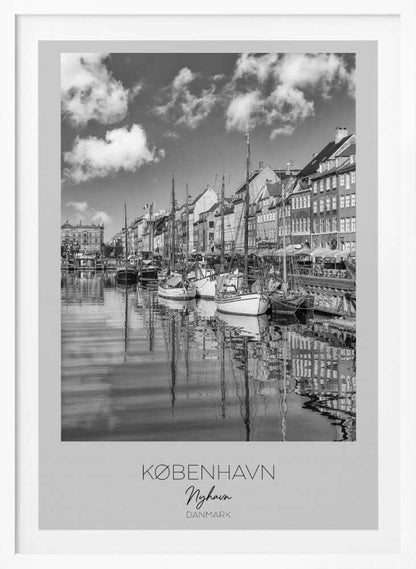 A black and white poster of Nyhavn harbor in Copenhagen. The photograph shows traditional sailboats and ships moored along a canal, with a line of historic, multi-story buildings on the far bank. The sky has fluffy clouds, and the entire scene is reflected in the calm water. The poster has a white border with the text 'KØBENHAVN', 'Nyhavn', and 'DANMARK' at the bottom, and is shown within a black frame. Poster
