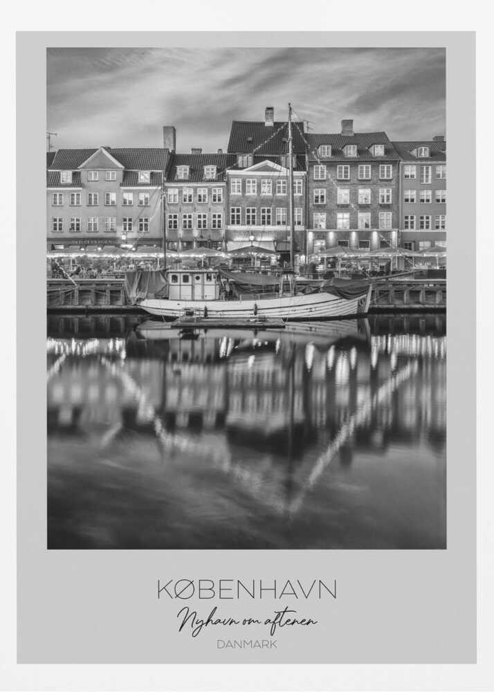 A black and white poster of Nyhavn harbor in Copenhagen at night. Historic buildings with glowing windows line the canal, and their lights create shimmering reflections in the water. A boat is docked in the foreground. The poster has text at the bottom that reads 'KØBENHAVN, Nyhavn om aftenen, DANMARK'. Poster