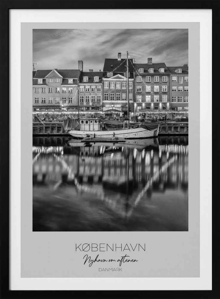 A black and white poster of Nyhavn harbor in Copenhagen at night. Historic buildings with glowing windows line the canal, and their lights create shimmering reflections in the water. A boat is docked in the foreground. The poster has text at the bottom that reads 'KØBENHAVN, Nyhavn om aftenen, DANMARK'. Poster