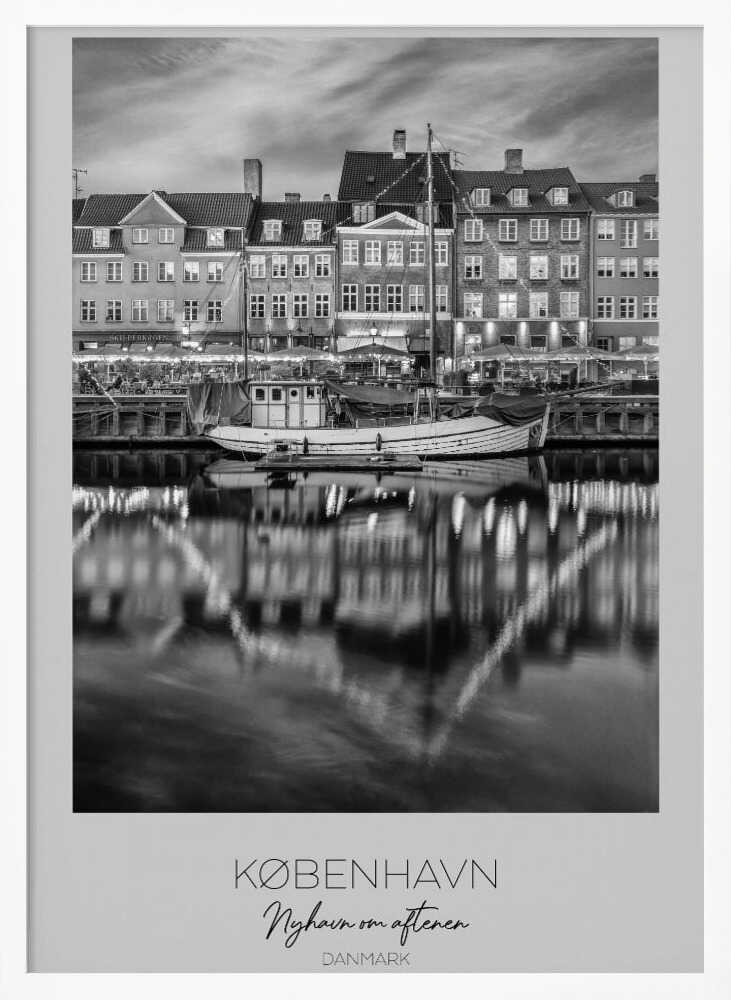 A black and white poster of Nyhavn harbor in Copenhagen at night. Historic buildings with glowing windows line the canal, and their lights create shimmering reflections in the water. A boat is docked in the foreground. The poster has text at the bottom that reads 'KØBENHAVN, Nyhavn om aftenen, DANMARK'. Poster