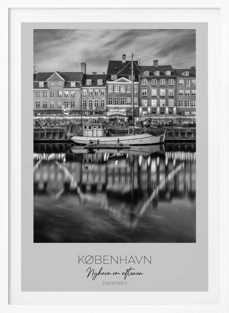 A black and white poster of Nyhavn harbor in Copenhagen at night. Historic buildings with glowing windows line the canal, and their lights create shimmering reflections in the water. A boat is docked in the foreground. The poster has text at the bottom that reads 'KØBENHAVN, Nyhavn om aftenen, DANMARK'. Poster
